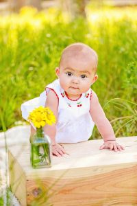 Kind in weißem Kleid mit Blumenvase vor sich