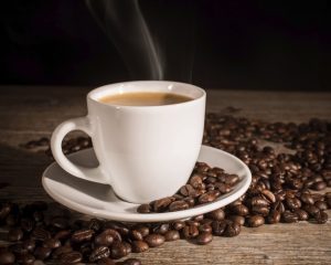 Eine Tasse dampfender Kaffee umgeben von Kaffeebohnen