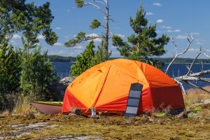 Orangefarbenes Zelt und Kajak am Ufer eines Sees