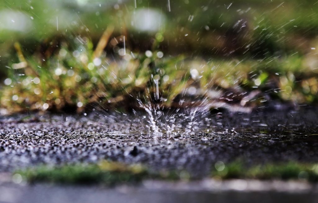 Regentropfen,, die auf durchnässten Boden treffen